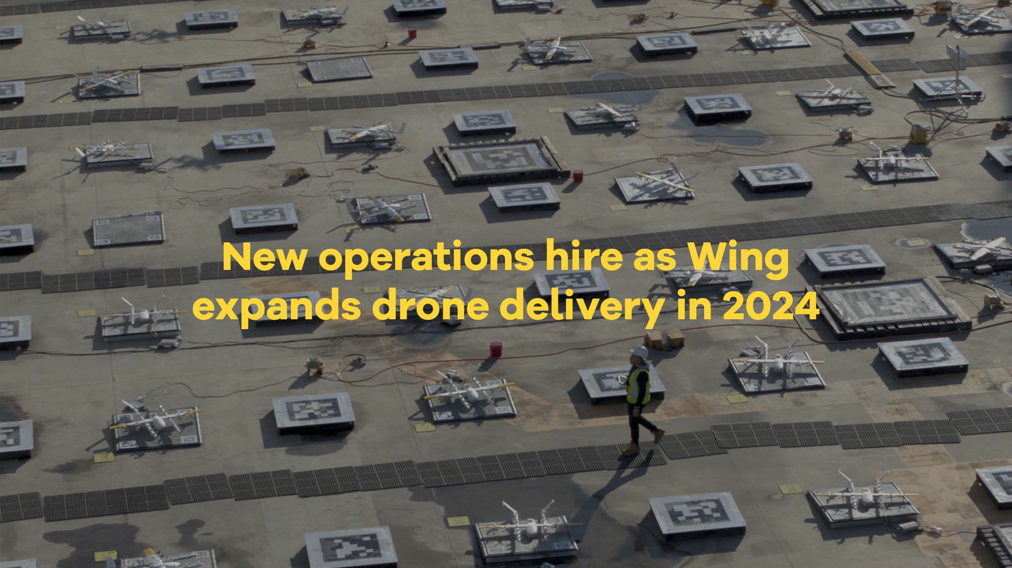 The image shows several drones arranged on a large grid-like platform with a person walking nearby, accompanied by text announcing a new operations hire as Wing expands its drone delivery in 2024.