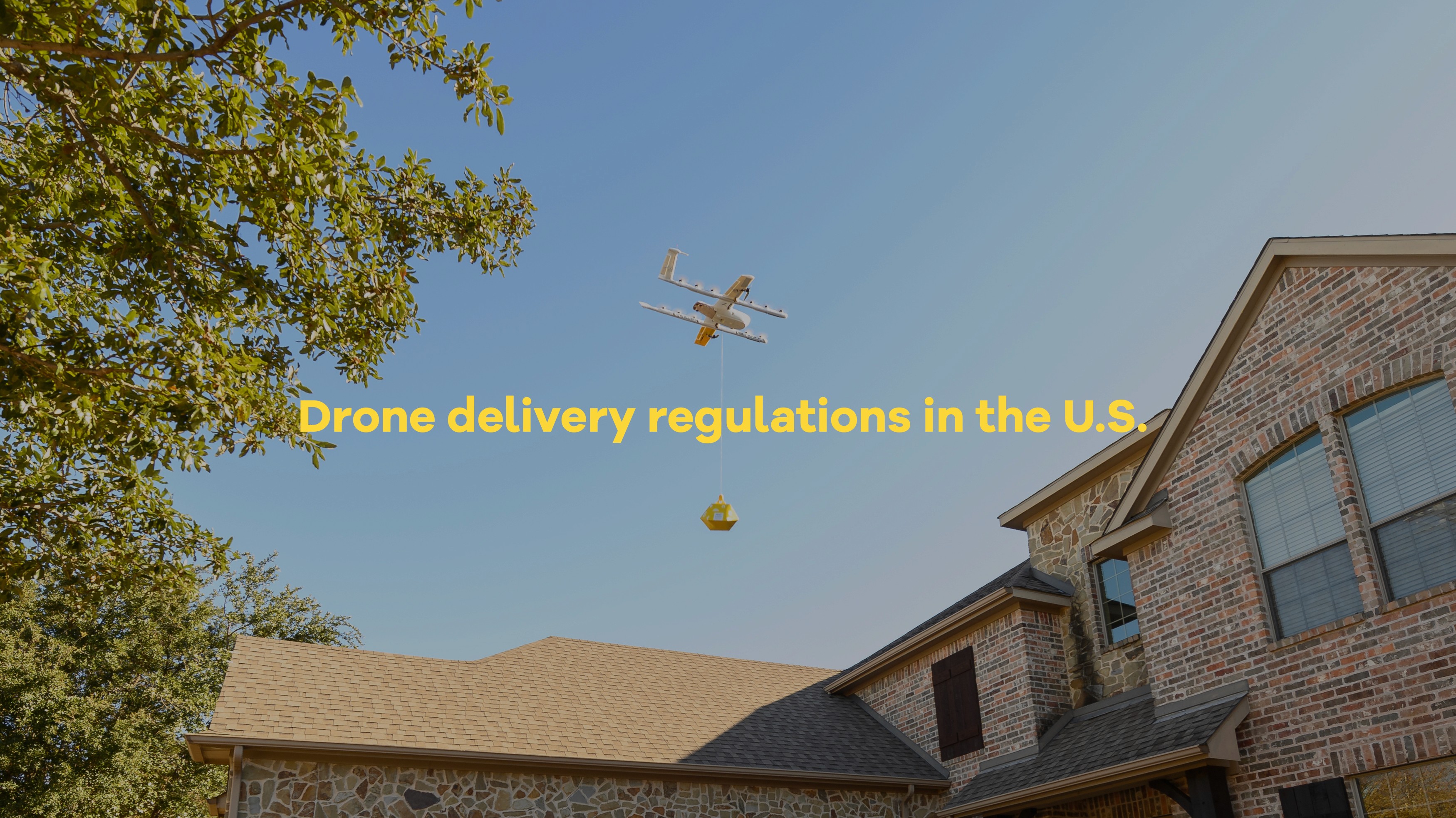 A delivery drone hovers in a clear blue sky, transporting a package above a suburban neighborhood with trees and a brick house visible.