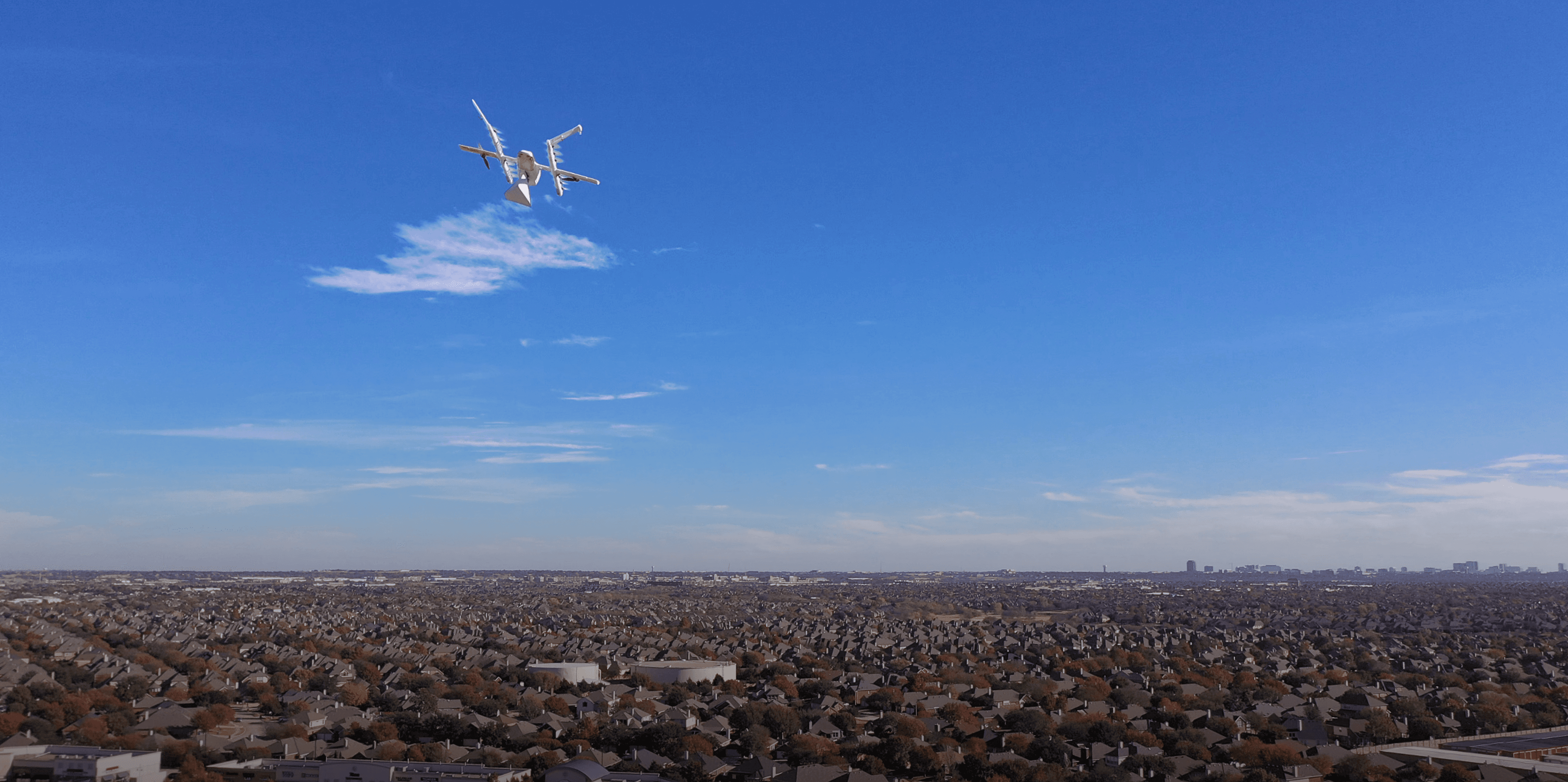A delivery drone flies over a sprawling suburban neighborhood under a clear blue sky, showcasing modern technology in urban logistics and transport.